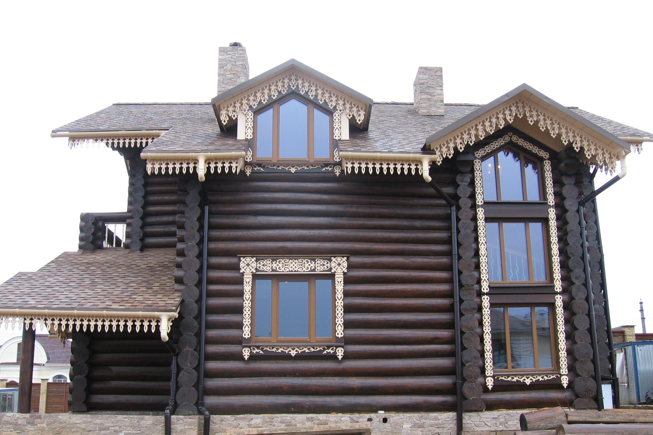 Светлые резные наличники и карнизы на темном фасаде деревянного дома
