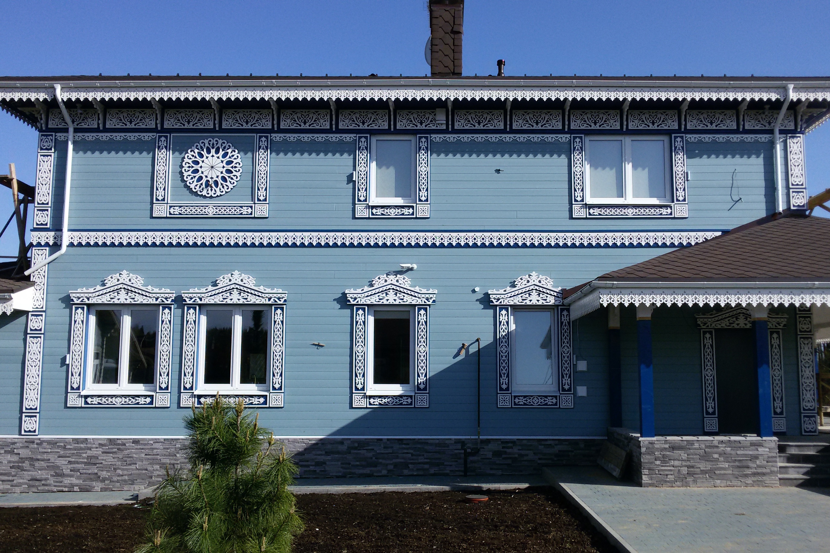 Монтаж светлых резных наличников и карнизов на голубом деревянном фасаде